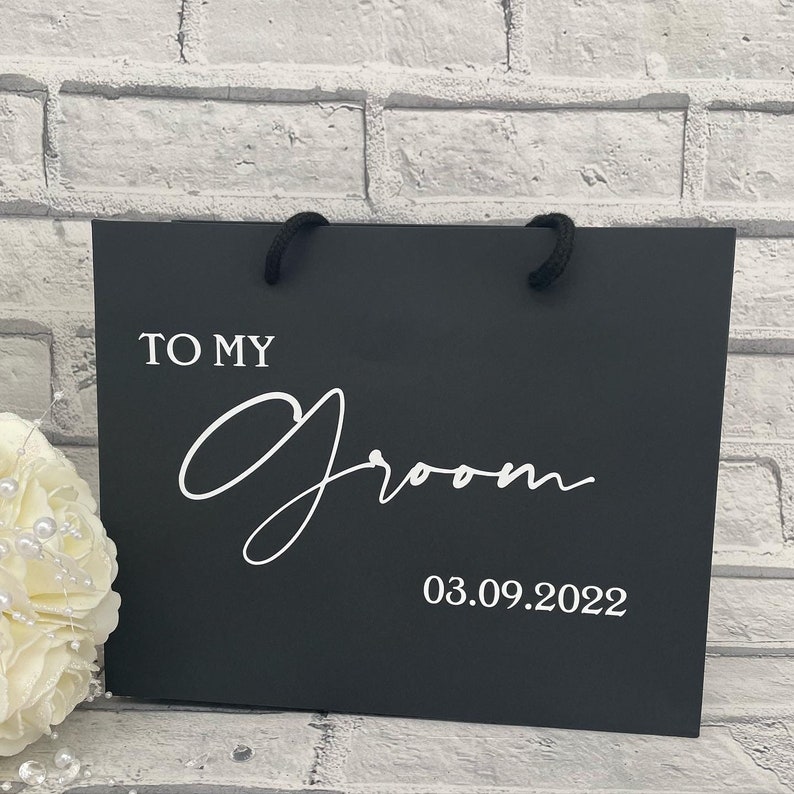 May include: Black gift bag with white text that reads "To My Groom 03.09.2022".