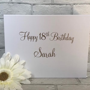 May include: White card with the text "Happy 18th Birthday Sarah" in brown cursive lettering.