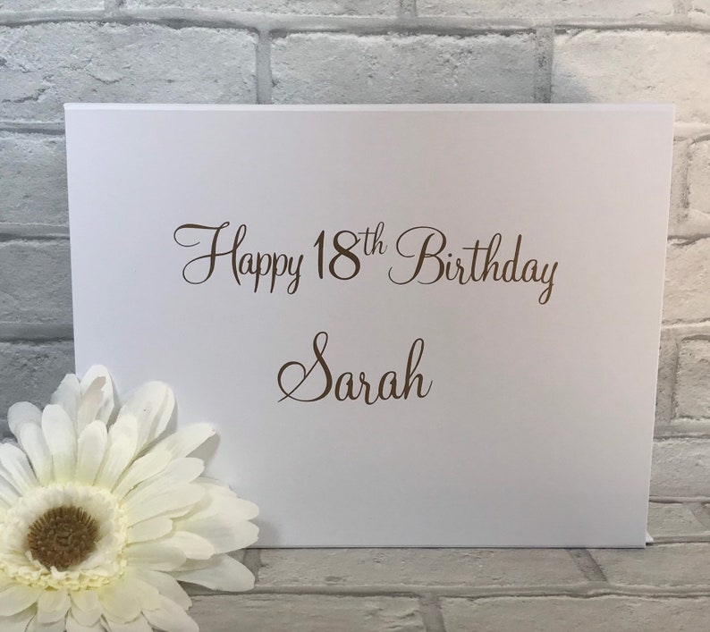 May include: White card with the text "Happy 18th Birthday Sarah" in brown cursive lettering.