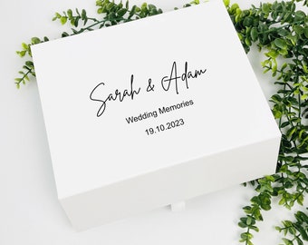 May include: White box with the text "Sarah & Adam" in black cursive script, "Wedding Memories" in black text, and "19.10.2023" in black text.