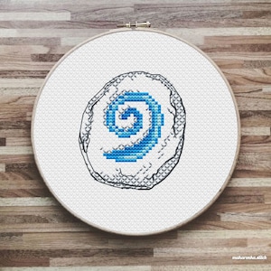 May include: A white embroidery hoop with a blue and white spiral design stitched on white fabric. The spiral is outlined in black thread.