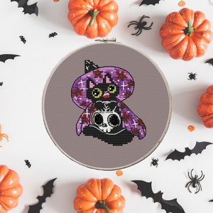 May include: A black cat wearing a purple and red witch hat with a skull design. The cat is sitting on a gray background. The image is surrounded by pumpkins and bats.