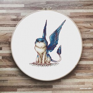 May include: Cross stitch pattern of a blue and white winged creature with a long tail, sitting on a white background.