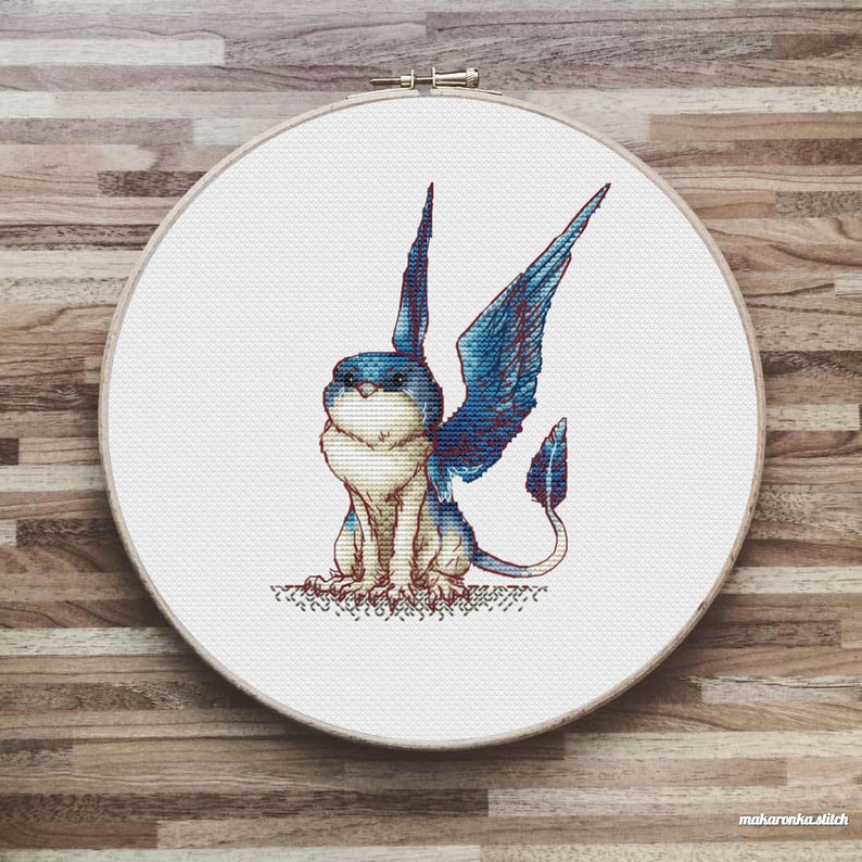 May include: Cross stitch pattern of a blue and white winged creature with a long tail, sitting on a white background.