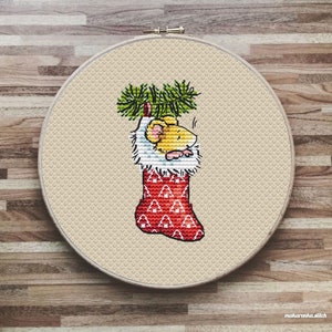 May include: A cross-stitch pattern of a yellow mouse in a red Christmas stocking with a green pine branch on top.