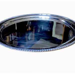 May include: A large, round, silver serving tray with a decorative, raised edge.