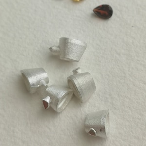 May include: Five silver metal pendant bails, each with a unique shape and design. The bails are arranged on a white surface.