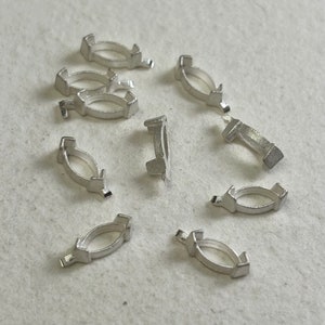 Peut inclure: Un ensemble de dix sertis de bélière en métal argenté pour la fabrication de bijoux. Les bélières sont de forme ovale et ont une finition lisse et polie.