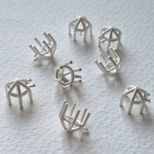 Könnte beinhalten: Acht silberne Ringfassungen für die Schmuckherstellung. Die Fassungen sind in verschiedenen Formen und Größen, einige haben eine runde oder quadratische Basis und andere eine spitze Oberseite.
