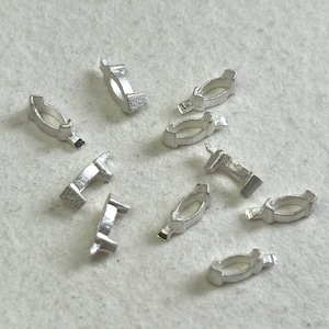 May include: Ten silver-colored metal rings, some oval-shaped and some rectangular, are scattered on a white surface.