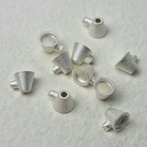 Peut inclure: Dix perles en métal de couleur argentée en forme de tasse. Les perles ont une surface texturée et un petit trou en haut.