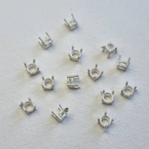 Può includere: Un set di 14 montature in metallo color argento per pietre preziose. Le montature sono rotonde e hanno quattro griffe.