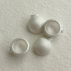 Puede incluir: Cuatro adornos de metal de color plateado en forma de cúpula con una superficie texturizada. Los adornos tienen una pequeña abertura en el lateral.