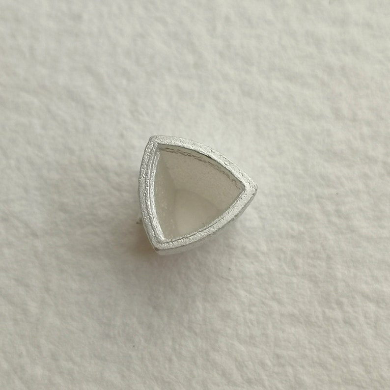 May include: A silver triangular bezel setting for a gemstone.