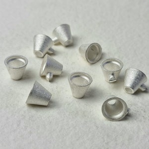 Könnte beinhalten: Zehn silberfarbene Metallkegel mit einer glatten, strukturierten Oberfläche. Die Kegel sind klein und haben eine abgerundete Spitze.