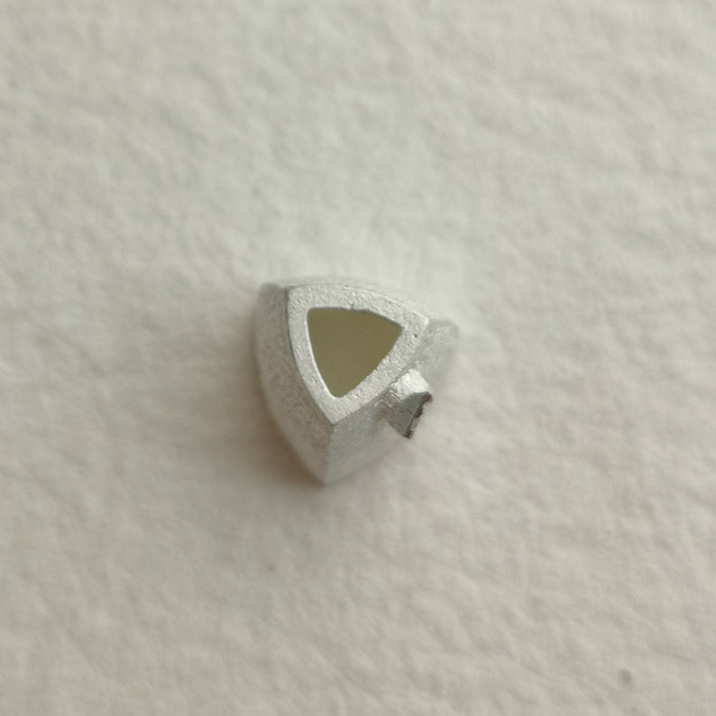 May include: A silver triangular pendant with a hollow center. The pendant has a smooth, metallic finish.