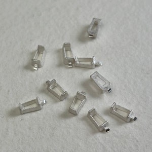 May include: A collection of ten silver-coloured metal pieces, each with a rectangular shape and a small opening. The pieces are arranged on a white surface.