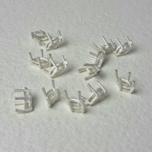 May include: A group of 10 silver-colored metal settings for oval-shaped gemstones. The settings are designed to hold the gemstones securely in place.