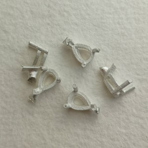 May include: Four silver-coloured metal settings for a pear-shaped gemstone. The settings have a prong setting and a loop for attaching a chain or bail.