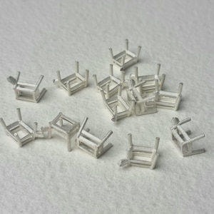 Puede incluir: Un grupo de 14 engastes de metal plateado para montar piedras preciosas. Los engastes son de forma rectangular con cuatro garras a cada lado.