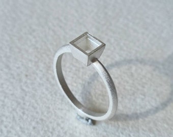 May include: A silver ring with a square-shaped setting for a gemstone. The setting is open and ready to be filled with a stone.