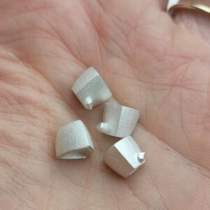 May include: Four silver-colored metal pieces with a textured surface. Each piece has a pointed tip and a slightly rounded base.