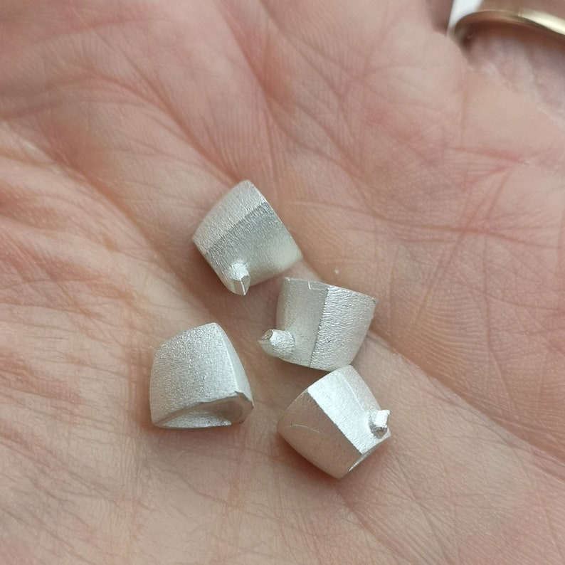 May include: Four silver-colored metal pieces with a textured surface. Each piece has a pointed tip and a slightly rounded base.