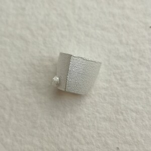 May include: A small, silver, geometrically shaped object with a textured surface.