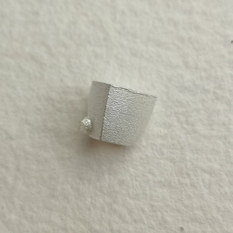 May include: A small, silver, geometrically shaped object with a textured surface.