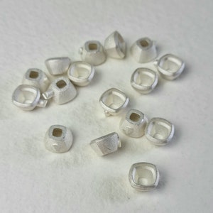 May include: A collection of 15 silver-toned metal settings for bezel settings. The settings are square shaped with a raised lip around the opening.