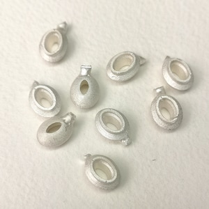 May include: Nine silver oval-shaped beads with a hole in the centre. The beads have a smooth, polished finish.