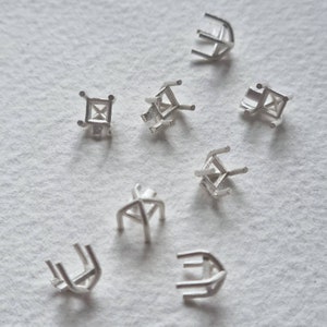 Puede incluir: Un conjunto de ocho engastes de metal plateado para montar piedras preciosas. Los engastes son de varias formas, incluyendo cuadrada, redonda y triangular.