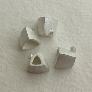 May include: Four silver-colored metal triangular shapes with a hollow center. The shapes are arranged in a circle on a white surface.