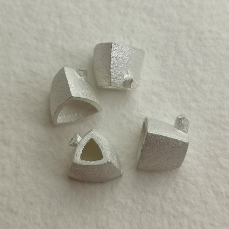 May include: Four silver-colored metal triangular shapes with a hollow center. The shapes are arranged in a circle on a white surface.