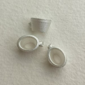 May include: Three silver metal rings with a smooth, polished finish. The rings are different sizes and shapes, with one being a cylinder and the other two being oval.