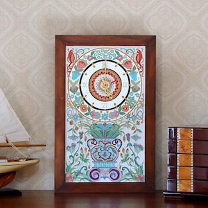 Puede incluir: Un reloj de pared enmarcado con un diseño floral colorido y una esfera blanca con números romanos negros. El reloj está rodeado por un marco de madera.