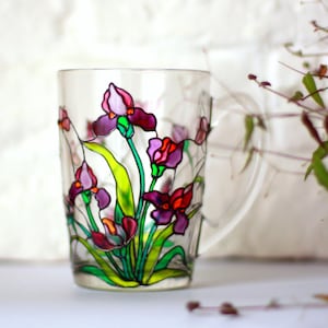 May include: A clear glass mug with a hand-painted design of purple, pink, and green iris flowers.