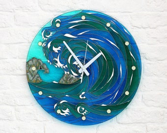 Può includere: Un orologio rotondo in vetro colorato blu e verde con un design a onda bianca. Il quadrante dell'orologio ha lancette bianche e accenti dorati.