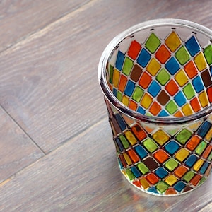 Peut inclure: Un bougeoir en verre transparent avec un motif en diamant coloré. Le motif comprend des nuances d'orange, de jaune, de vert, de bleu et de marron.