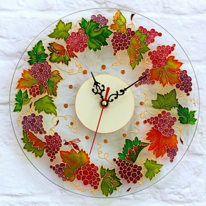 May include: A round glass clock with a white face and black hands. The clock is decorated with a painted design of grapes and leaves in shades of green, purple, red, and orange.