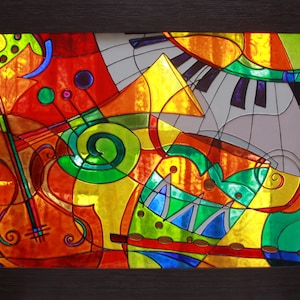 Op de afbeelding: Abstracte glas-in-lood kunstwerk met een kleurrijk ontwerp van muziekinstrumenten, waaronder een viool, pianotoetsen en een trompet. Het kunstwerk is ingelijst in een donkerhouten lijst.