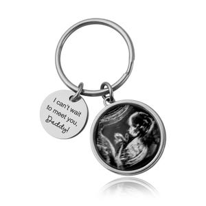 May include: A silver keychain with two charms. One charm is a round disc with the text "I can't wait to meet you, Daddy!". The other charm is a round pendant with a black and white sonogram image.