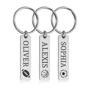 May include: Three silver keychains with rectangular tags. Each tag has a name and a sports-related icon: "OLIVER" with a football, "ALEXIS" with a basketball, and "SOPHIA" with a soccer ball. The keychains are on a white background.