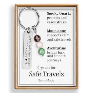 May include: A silver keychain with a rectangular tag engraved with "Drive safe handsome. I love you -K." The keychain features three gemstone beads: smoky quartz, moonstone, and aventurine. The card reads "Crystals for Safe Travels" and lists the benefits of each stone.
