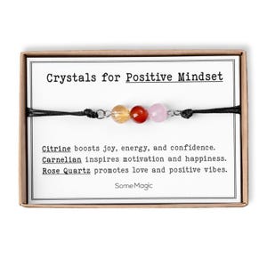 May include: A bracelet with citrine, carnelian, and rose quartz beads, presented in a box. The text on the card reads "Crystals for Positive Mindset." The card also lists the benefits of each crystal: joy, energy, confidence, motivation, happiness, love, and positive vibes.
