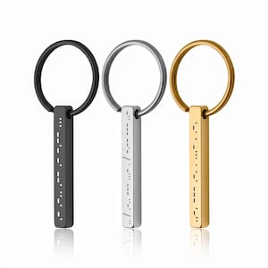 May include: Three metal keyrings in black, silver, and gold. Each keyring features a rectangular pendant with a Morse code pattern and a circular ring. The keyrings are displayed against a white background.