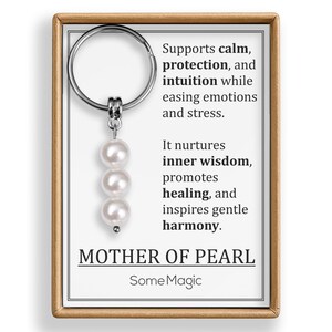 May include: A keychain with a silver ring and a pendant of three white pearls. The keychain is presented on a card with text that reads "Supports calm, protection, and intuition..." and "Mother of Pearl". The brand name "SomeMagic" is also visible.