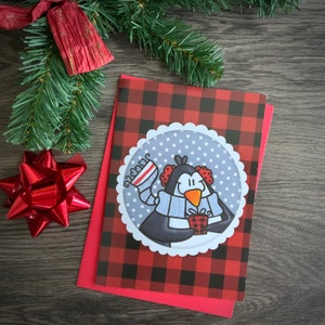 Jolie carte de souhait de Noël avec illustration d’un pingouin avec un cadeau, fond carreaux rouge/noir, Buffalo plaid.