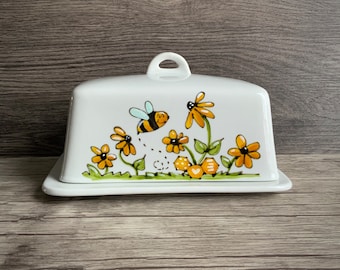 butter dish with bee, flowers and aveoles of honey, with flower and inscription Bzzz!!! in the back.