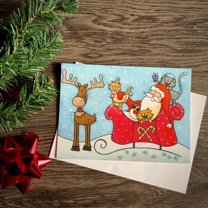 Jolie carte de souhait de Noël avec illustration d’un père Noël dans son traîneau avec des chats.
